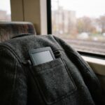 A small e-reader tucked into the pocket of a wool coat lying on a commuter train seat by a rainy window.